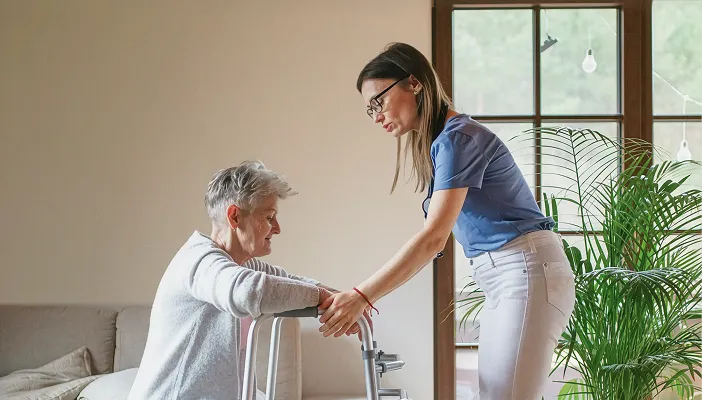 An occupational therapist supporting an older woman using a walking frame